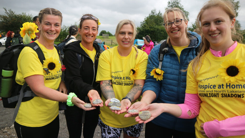 Walkers in yellow Hospice at Home Tshirts hold stones with in memory words on.